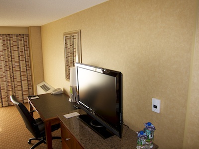 Wall of our hotel room, showing HVAC unit in the far corner and HVAC control panel close by, separated by a desk and TV console