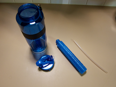 Disassembled water bottle, consisting of bottle body, screw-on lid with spout, cylindrical cooling element, and breather hose
