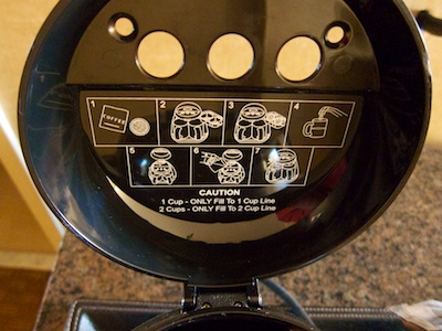 Lid of the coffee maker, lifted up, and displaying iconic brewing instructions on its inside