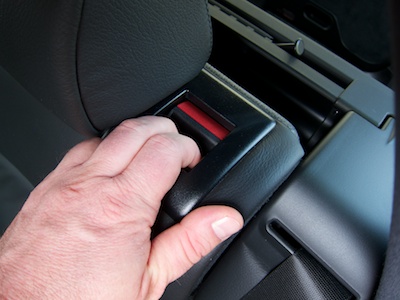 Hand on the rear seat back with two fingers inserted into the unlock handle and pulling the seat back towards the car's front.